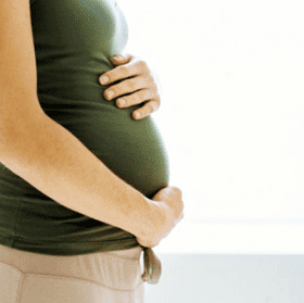 Side view of a pregnant woman in a green top gently holding her belly with both hands. - Olive Oil Times