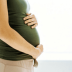 Side view of a pregnant woman in a green top gently holding her belly with both hands. - Olive Oil Times