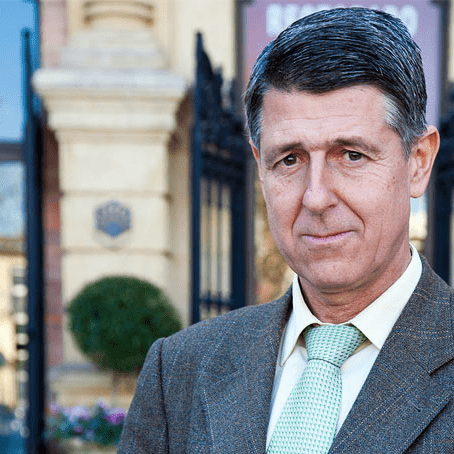 Man wearing a brown suit and a green tie, standing outdoors near a building entrance. - Olive Oil Times