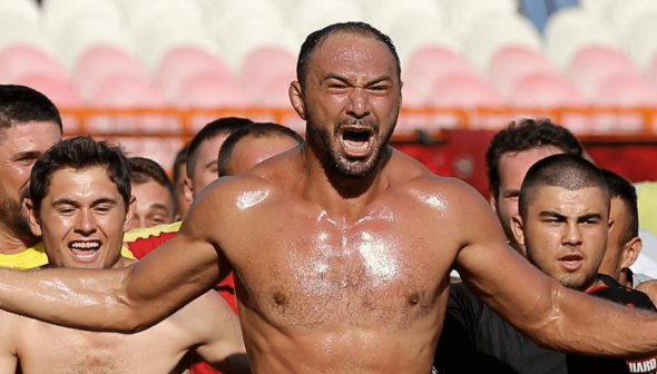 Group of enthusiastic fans celebrating at a sports event with one man prominently shouting. - Olive Oil Times