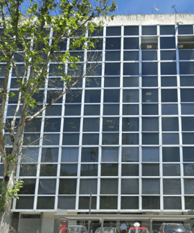 A modern office building featuring a grid pattern of large windows and a tree in front. - Olive Oil Times