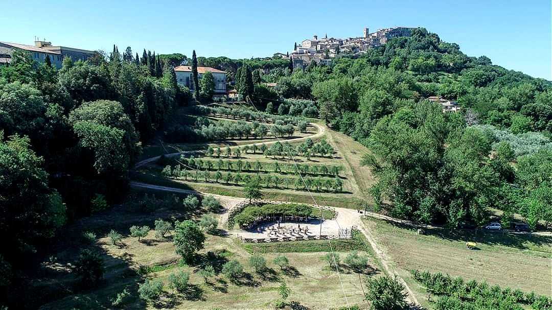 A hillside landscape features terraced gardens and a small settlement atop a hill, surrounded by green trees.
