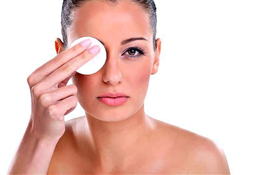 A woman uses a cotton pad to remove makeup from her face.