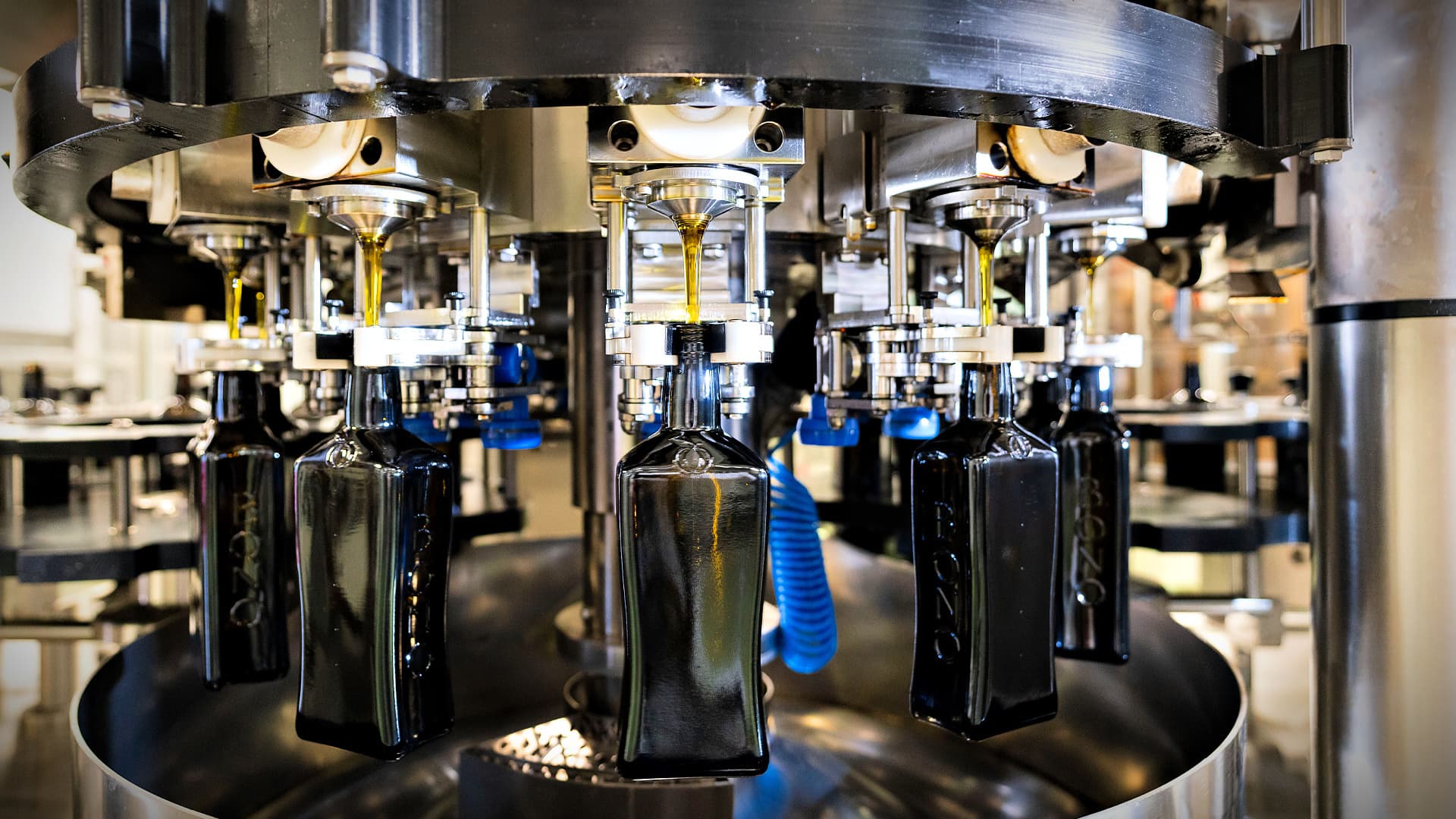 A close-up view of a bottling machine filling dark glass bottles with liquid.