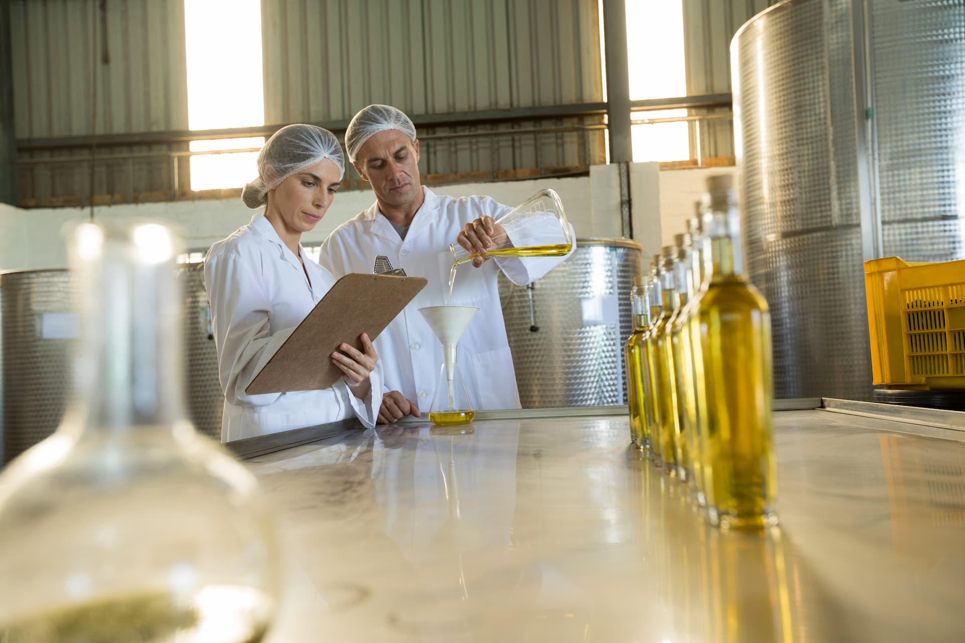 Two scientists in lab coats examine data while one pours liquid into a funnel in a research facility.