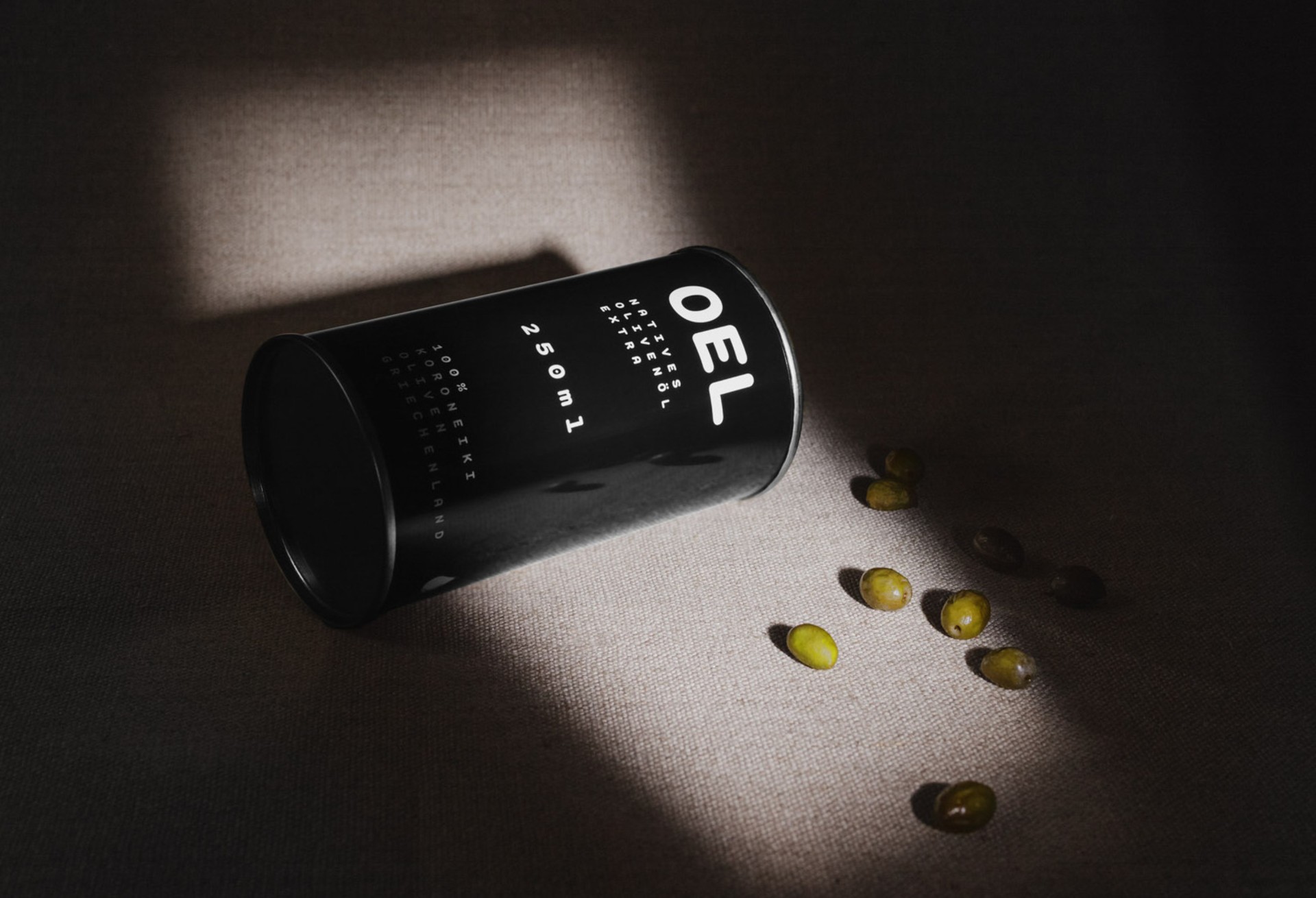 A black canister labeled "OEL" lies on a textured surface next to several green olives.