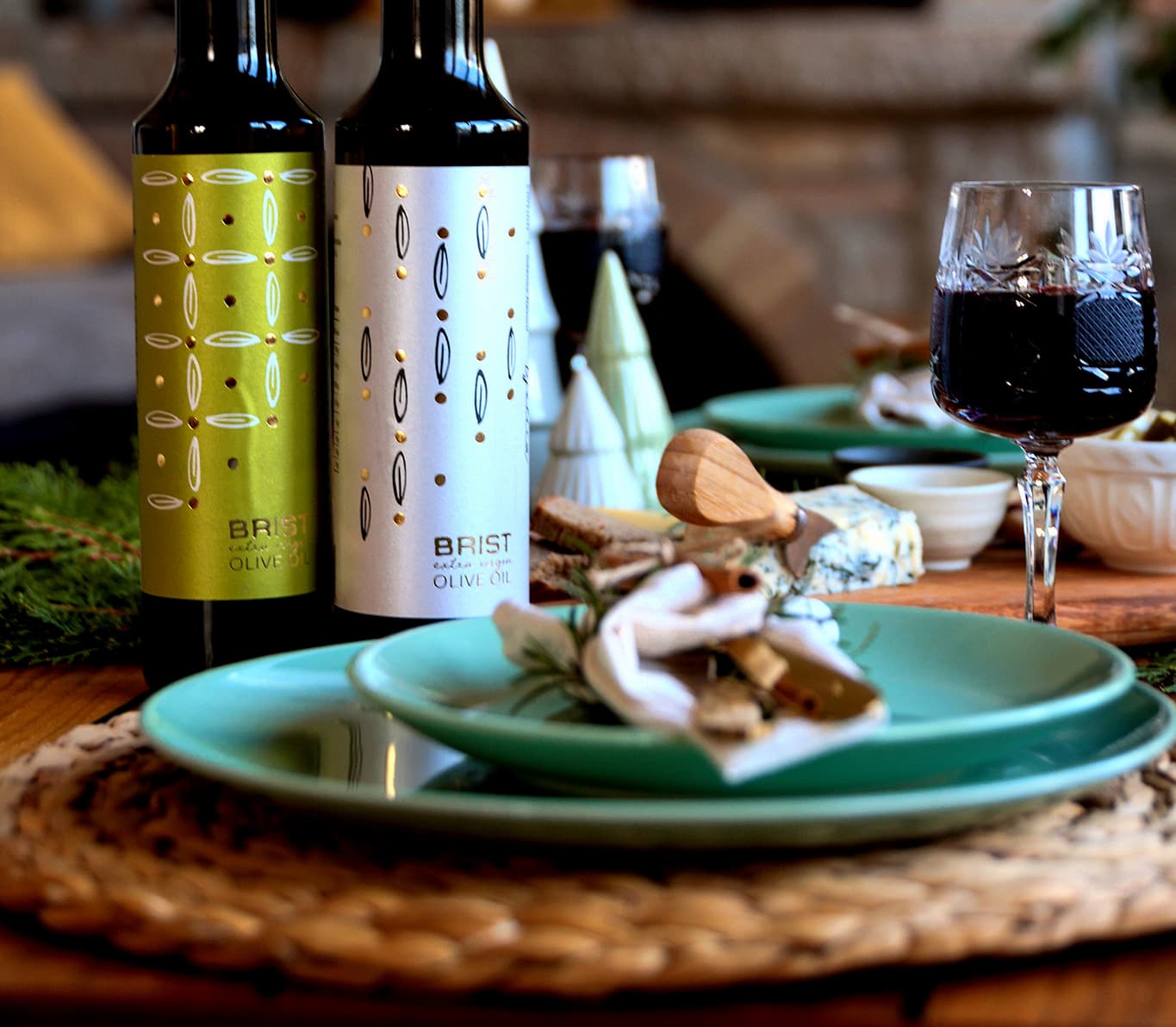 A dining table set with green and silver olive oil bottles, wine glasses, and assorted appetizers.