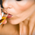 Close-up of a woman taking a sip from a small glass containing a golden liquid. - Olive Oil Times