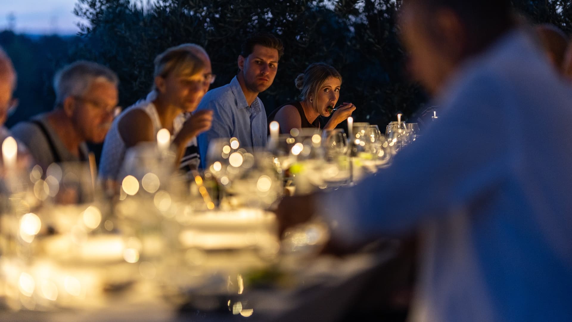 A group of people dining at a candlelit table during the evening, creating a warm, intimate atmosphere.