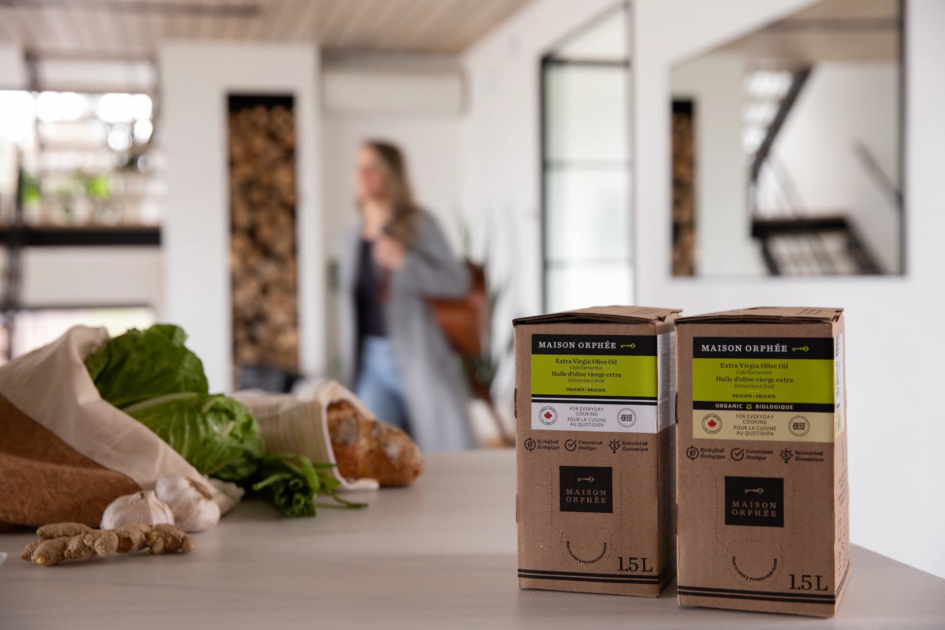 Two eco-friendly food packaging boxes sit on a table, with fresh produce and a blurred person in the background.
