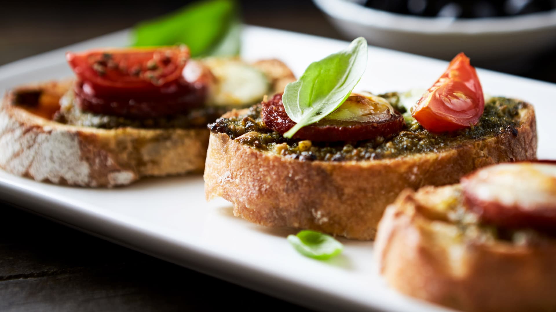 Three pieces of toast topped with pesto, tomatoes, and basil on a white plate.
