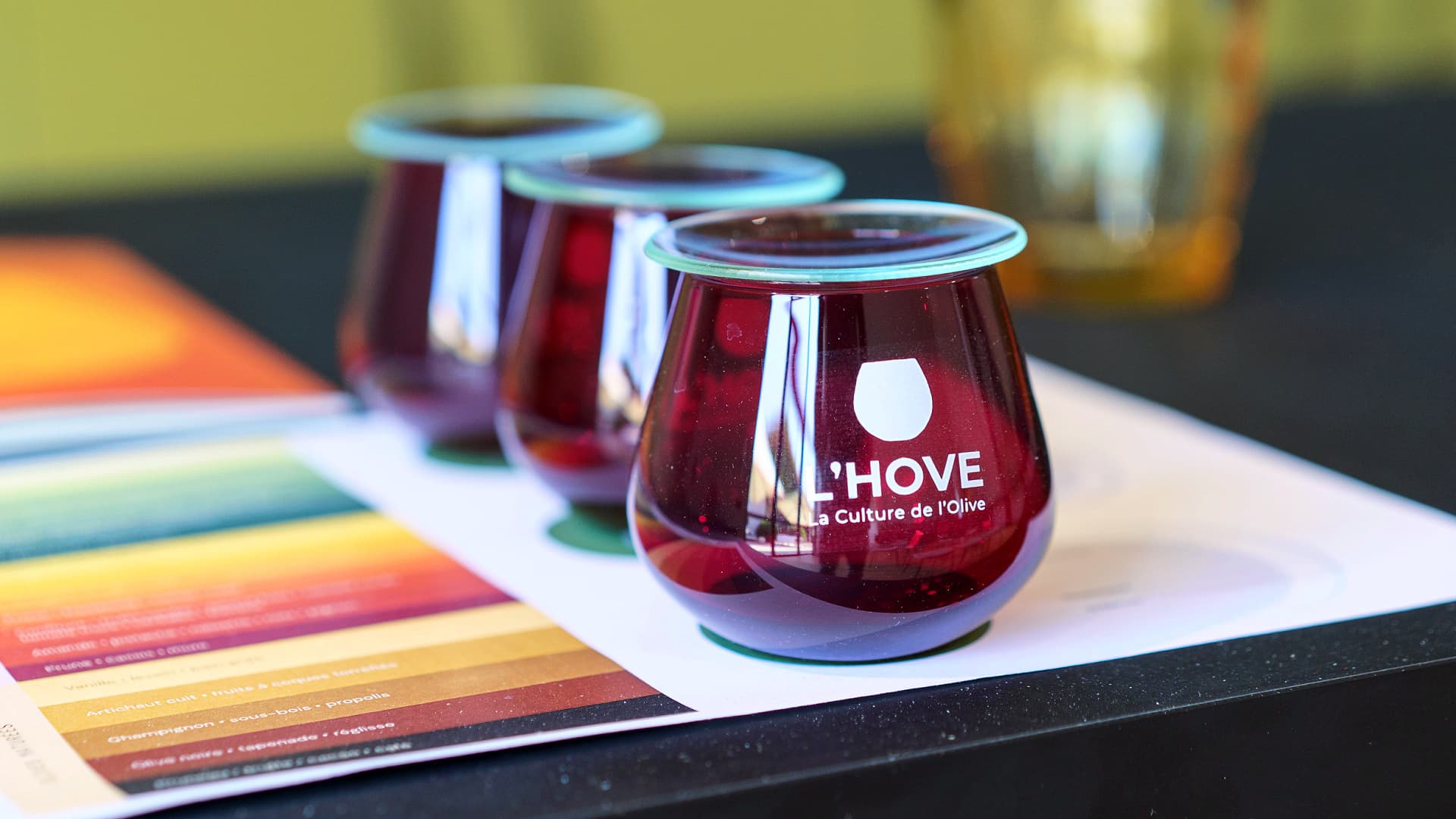 Three curved glass cups filled with olive oil sit on a table next to a color palette.